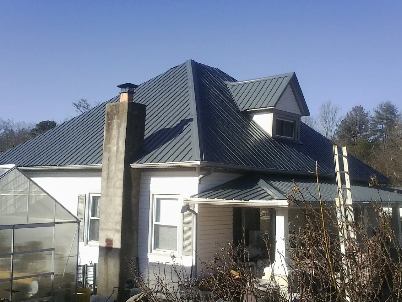 Dark blue standing seam metal roof on a white farmhouse with dormer — Slate & Tile Roof Repair by Roofing Brothers in Tomball