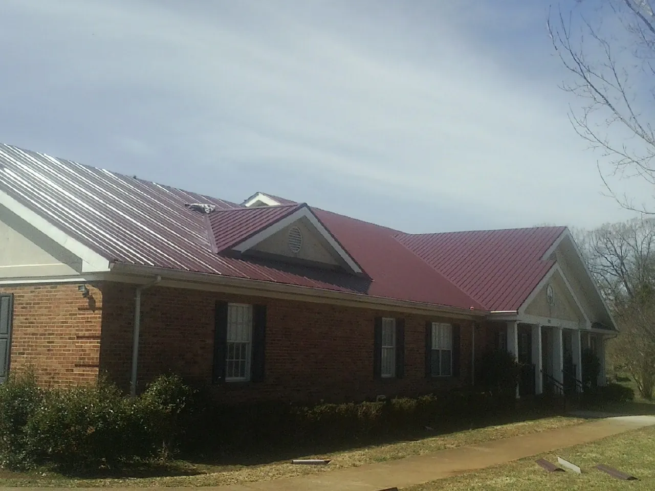 Red metal roof with gabled entries on a long brick building, from a Hail Damage Roof Repair job in Tomball
