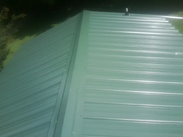 New green metal panels meeting at the ridge of a roof — Flat Roof Repair work by our crew in Tomball