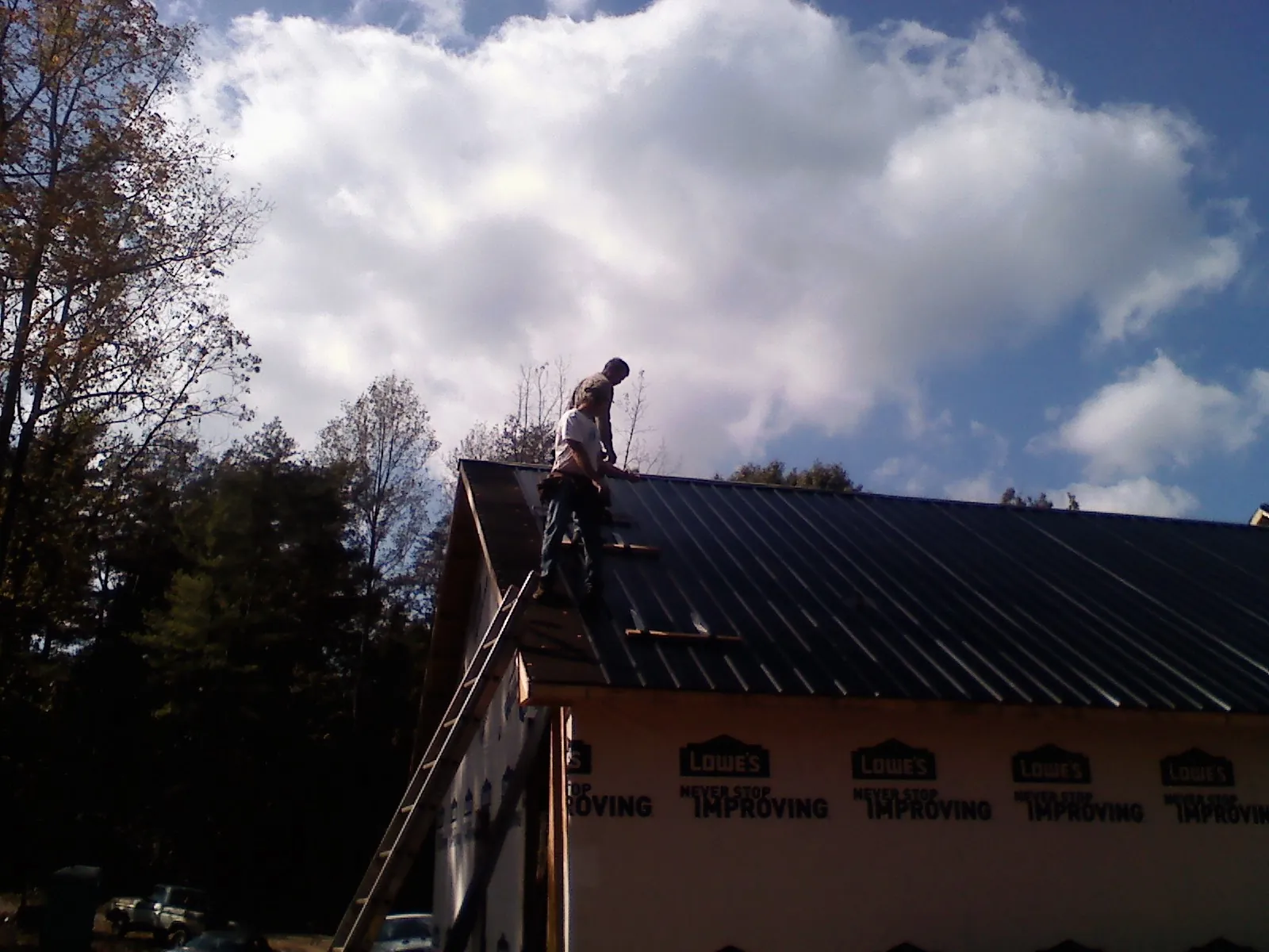 Roofer fastening dark metal panels high against a cloudy sky in Tomball