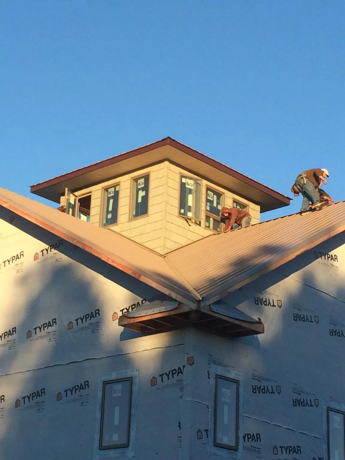 Roofers working around a rooftop cupola on a new metal roof at sunset — Roof Waterproofing in Tomball by Roofing Brothers